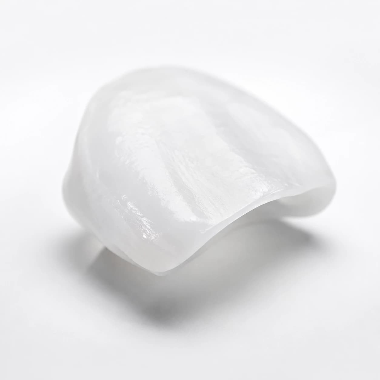 Thin porcelain dental veneer photographed on a bright minimal studio background